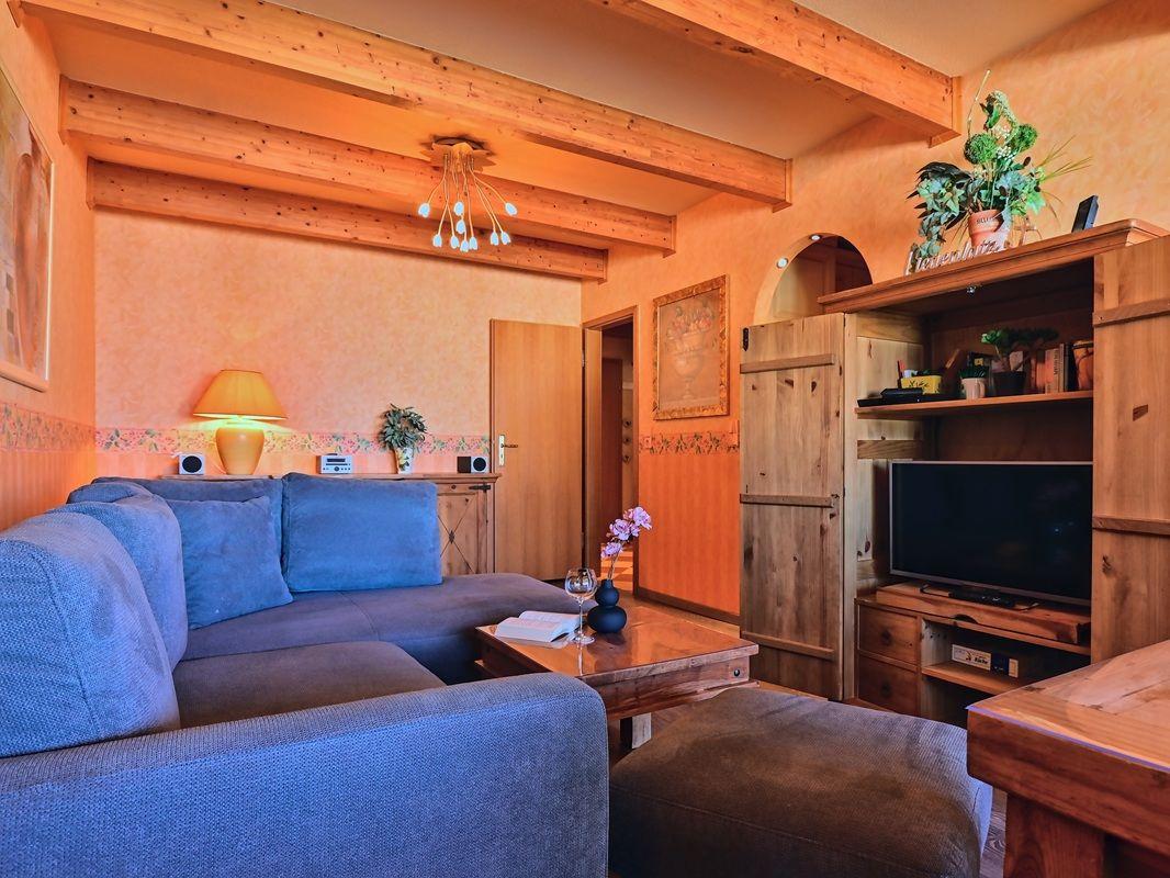 Wohnzimmer mit blauem Sofa, Holzregal und Fernseher.