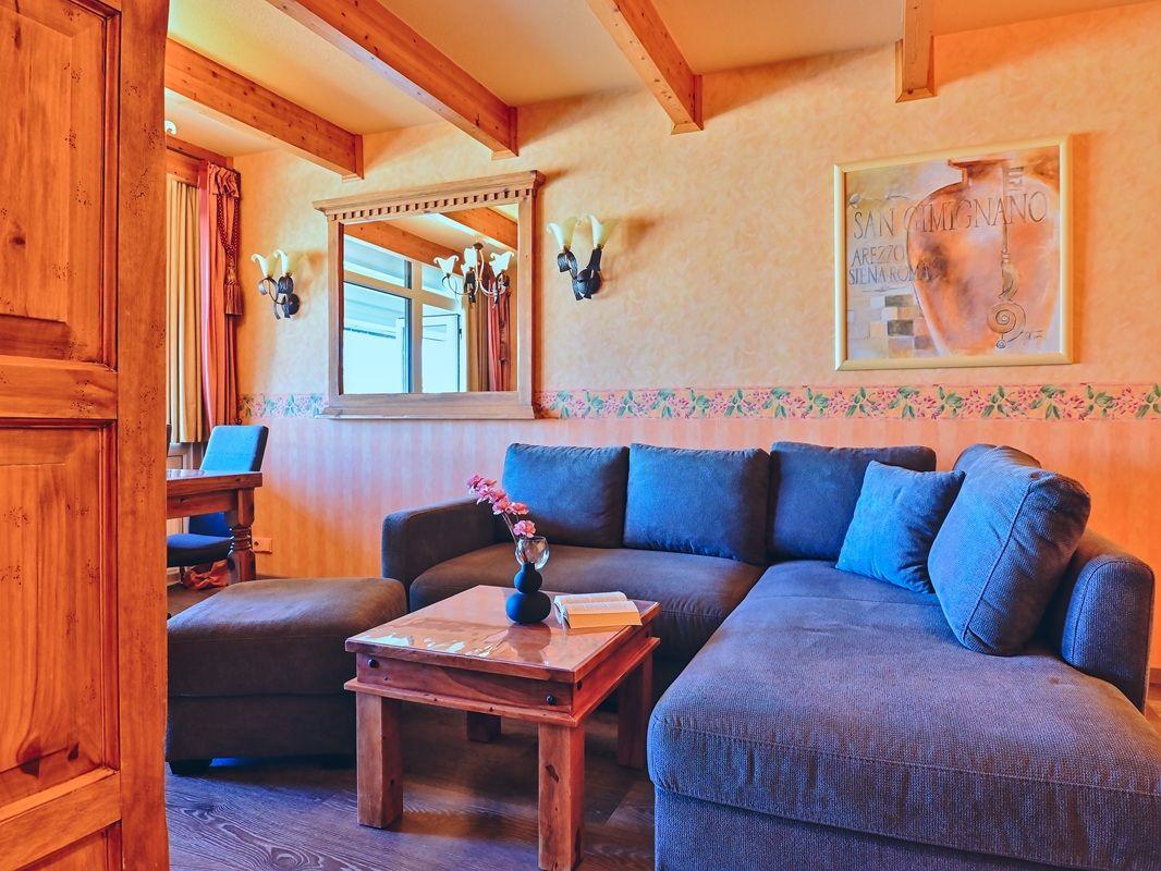 Wohnzimmer mit Sofa, Couchtisch und Wandspiegel. Holzbalken und Tapete mit Blumenmuster.