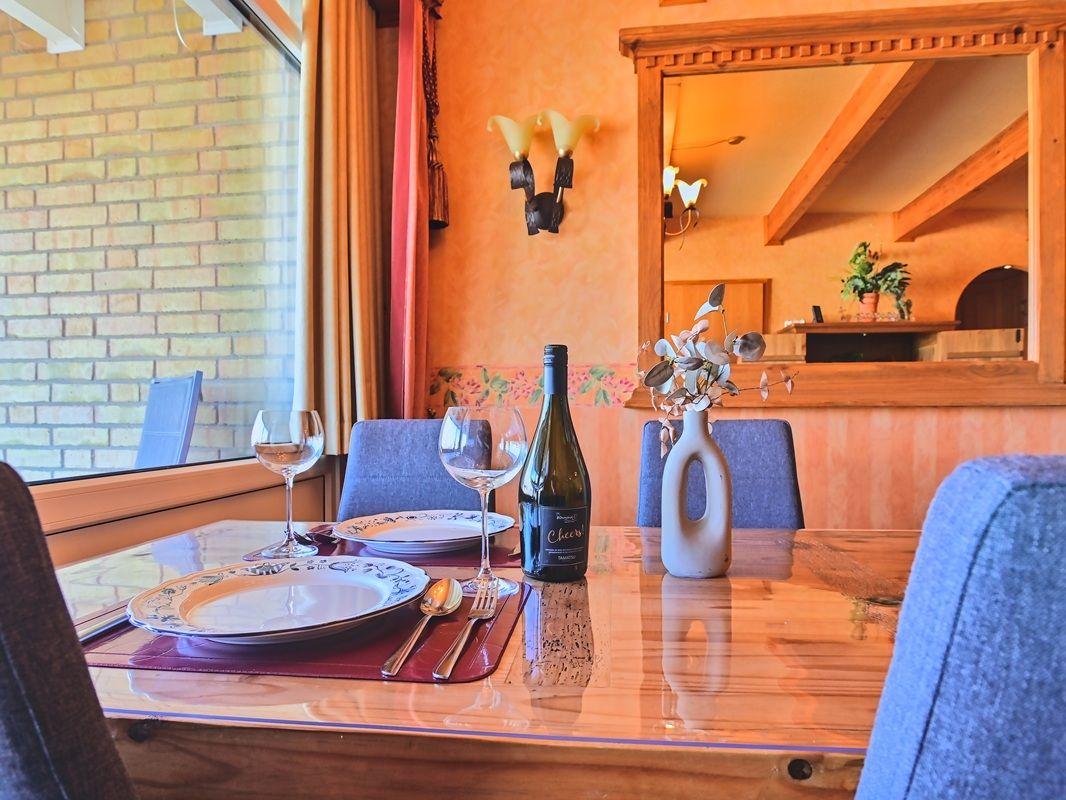 Esstisch mit Platz für vier Personen, Flasche Wein und Blumenvase.