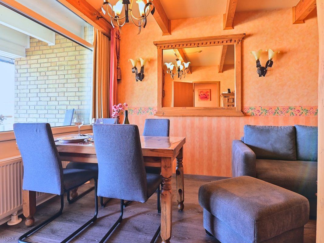 Esszimmer mit Holztisch, Stühlen und Sofa. Wand mit Spiegel und Lampen.