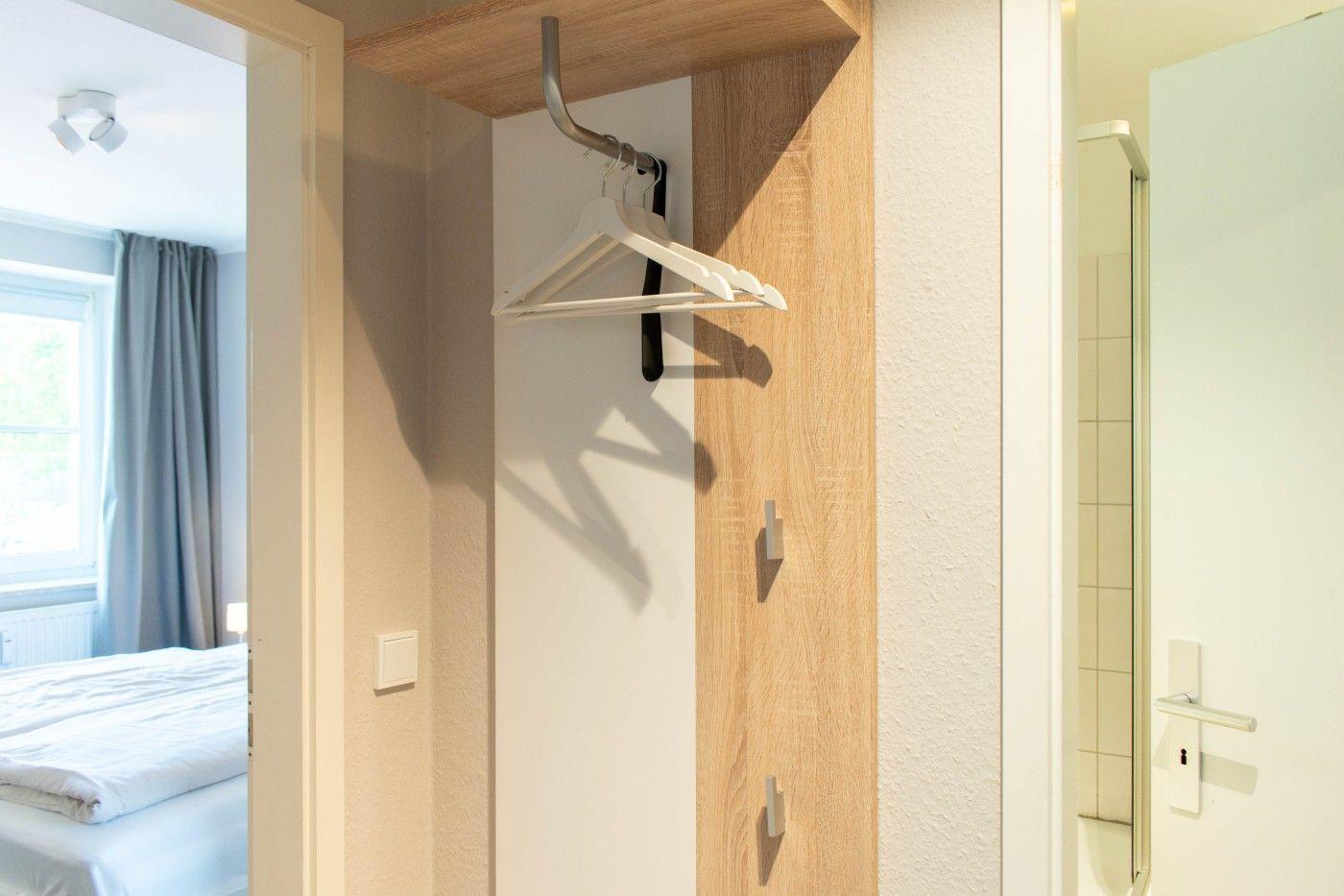 Schlafzimmer mit Bett und Fenster. Kleiderständer mit Haken. Tür zur Dusche.