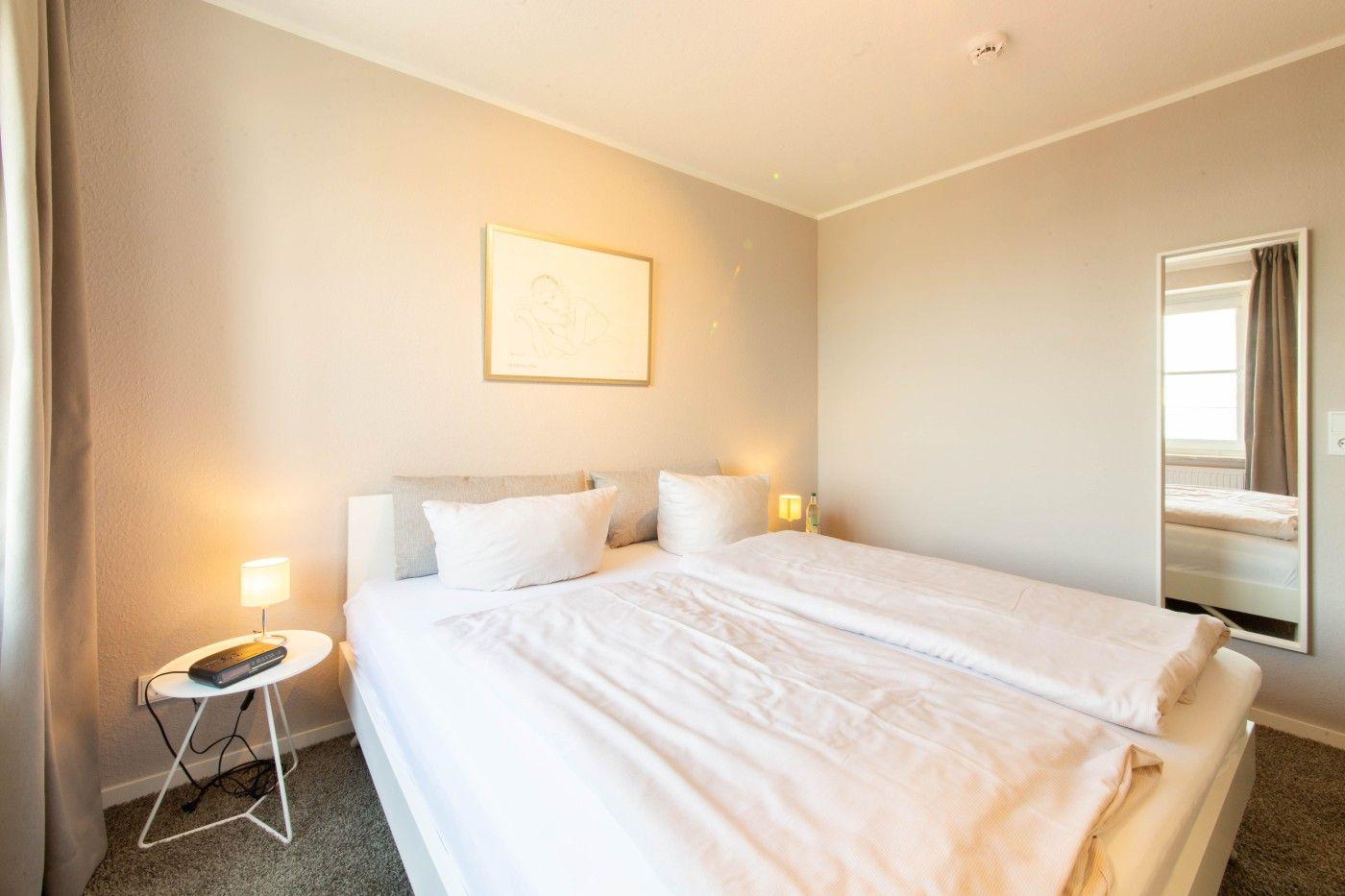 Schlafzimmer mit Doppelbett, Nachttisch und Spiegel an der Wand.