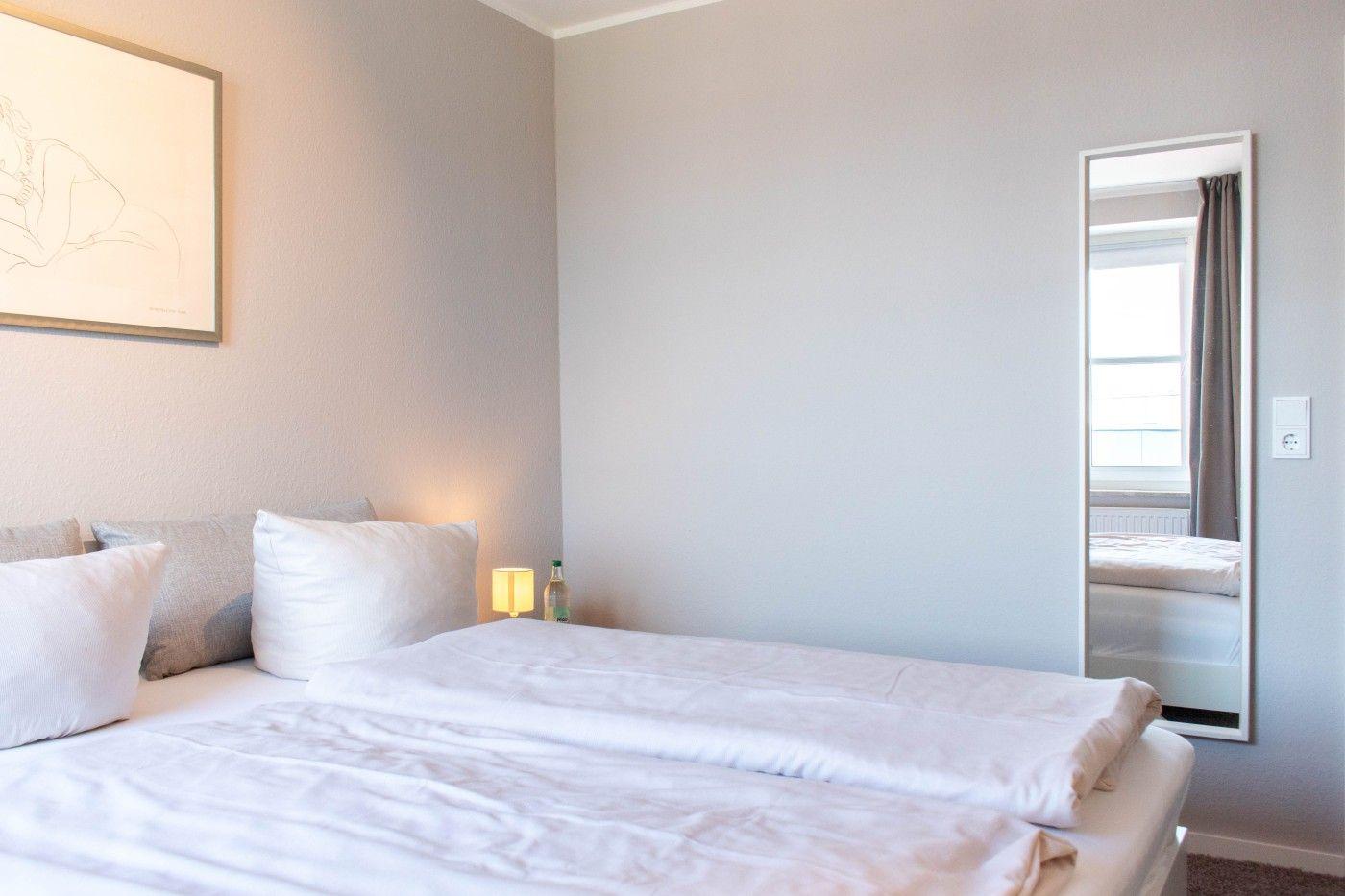 Schlafzimmer mit Bett, Wandspiegel und Wandbild. Neben dem Bett steht eine Lampe.