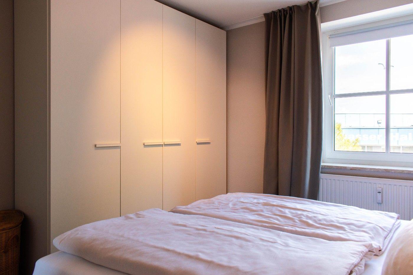 Schlafzimmer mit Doppelbett, Kleiderschrank und Fenster mit Vorhang.