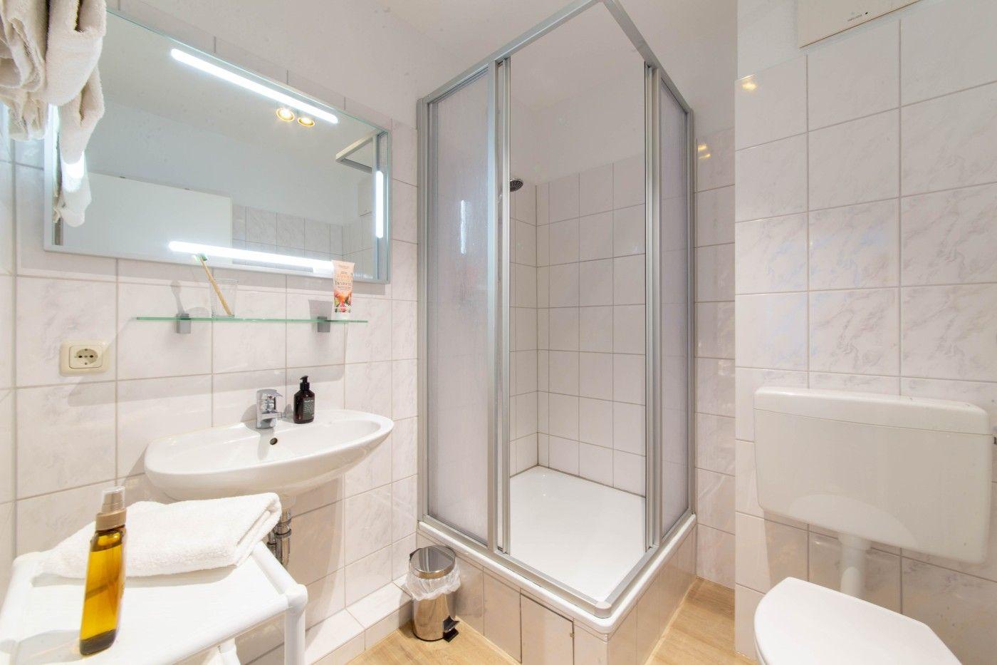 Badezimmer mit Dusche, Waschbecken und Toilette. Fliesenwand und Spiegelschrank.