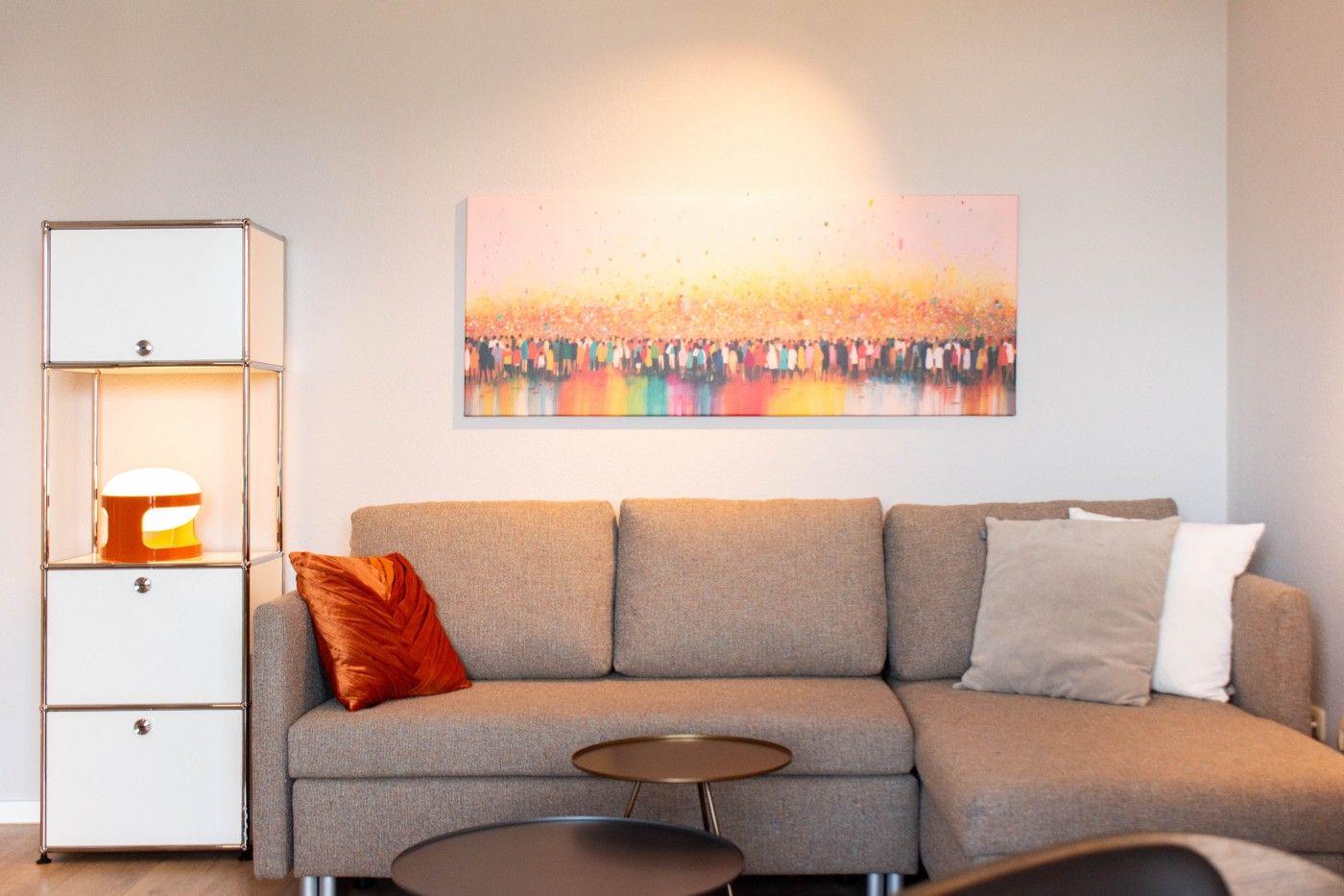 Ein grauer Sofa mit Kissen und einem Wandbild über dem Sofa.