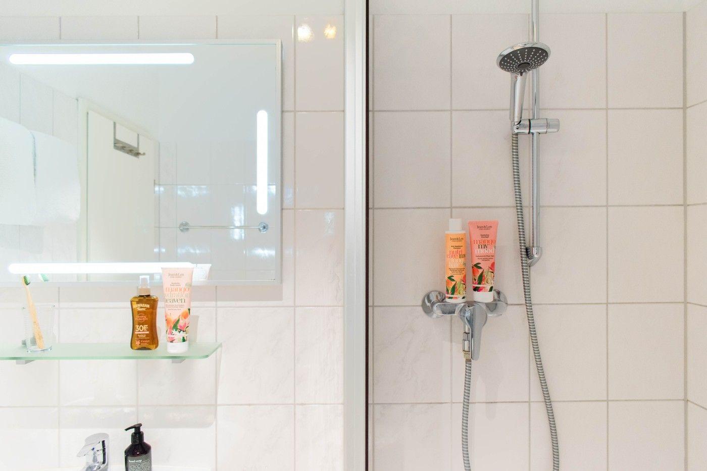 Badezimmer mit Dusche, Spiegel und Pflegeprodukten auf Ablagefläche.