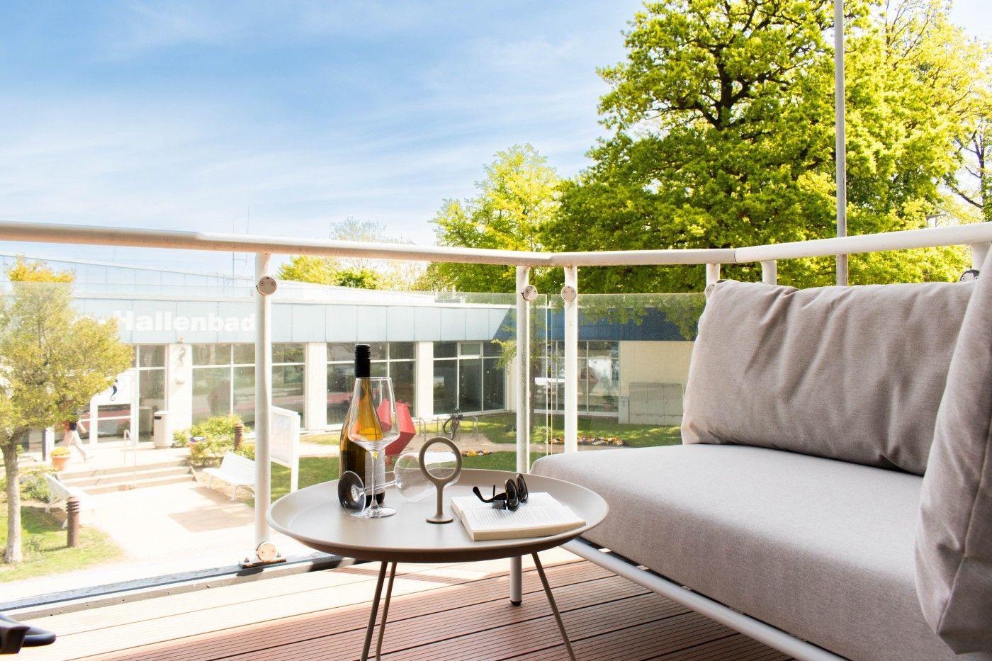 Terrasse mit Sofa und Tisch. Im Hintergrund Hallenbad und Bäume.