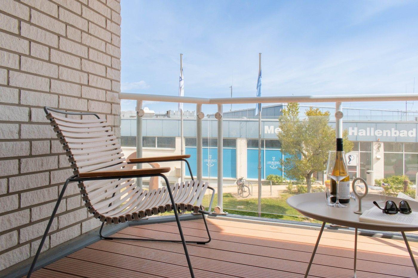 Terrasse mit Stuhl und Tisch. Im Hintergrund Hallenbad mit blauen Fenstern.