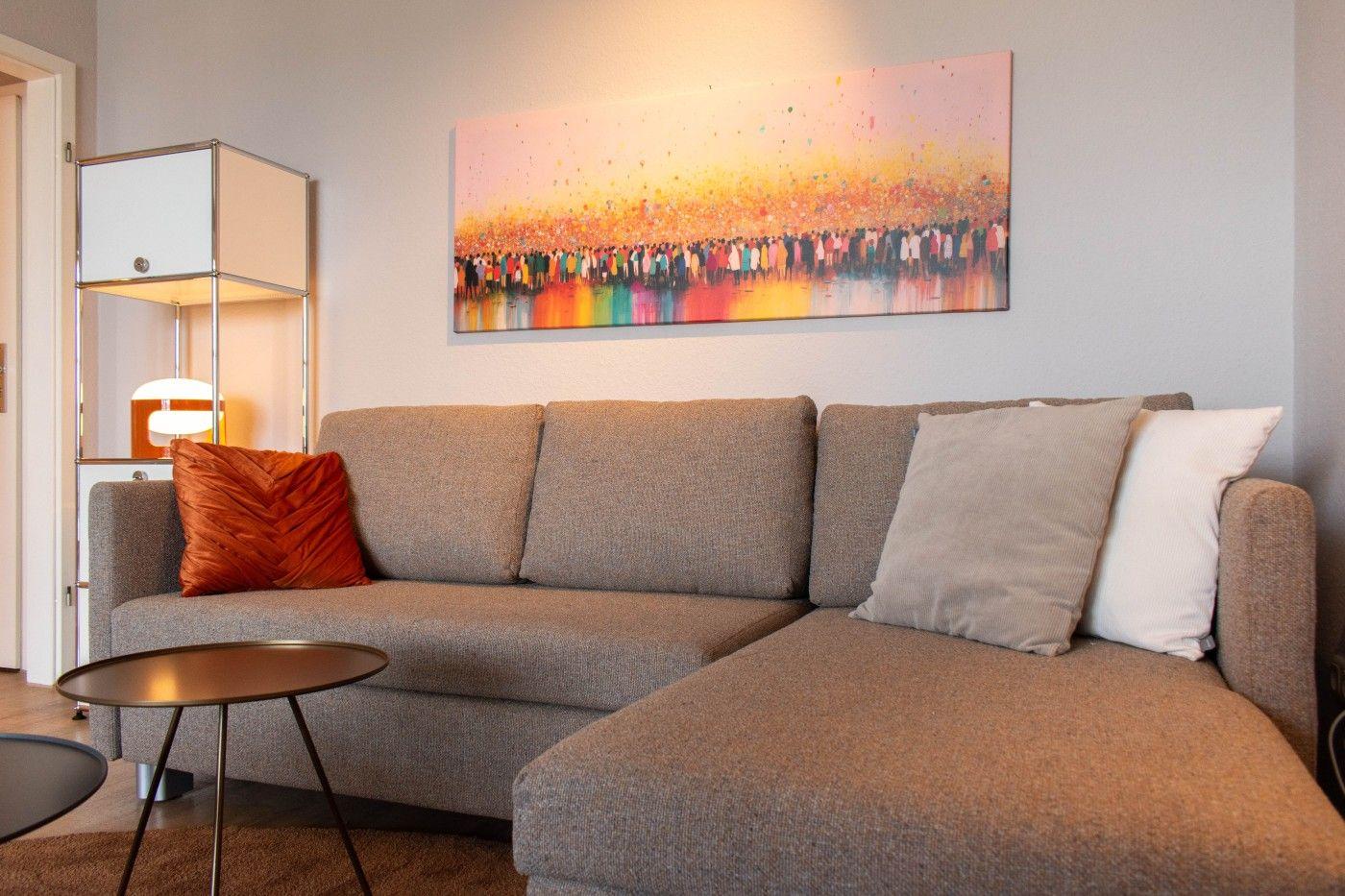 Ein grauer Sofa mit Kissen und einem runden Tisch. An der Wand hängt ein großes Bild.