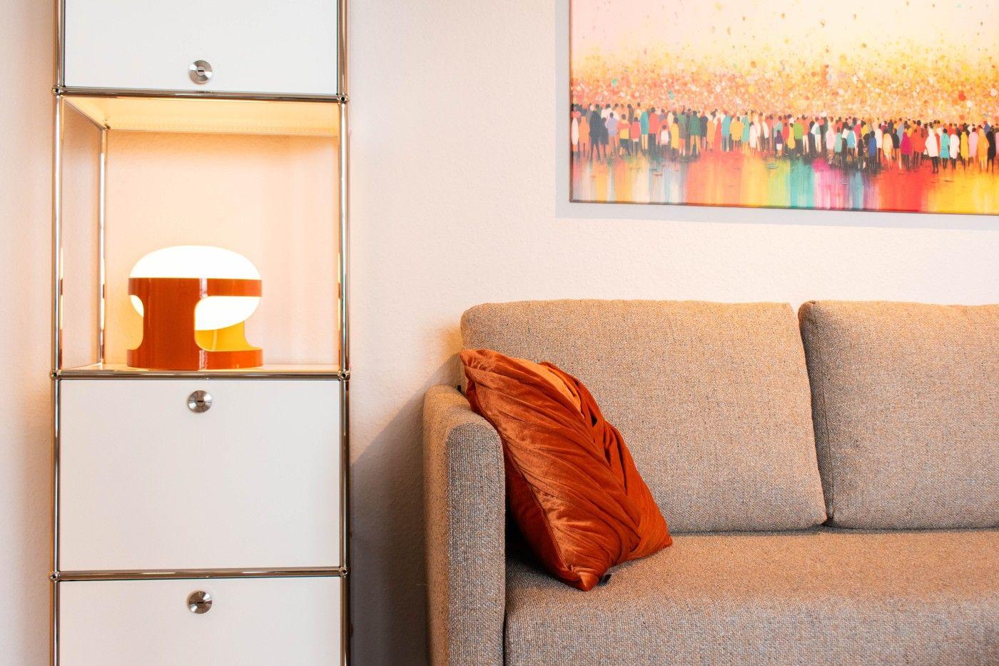 Ein Sofa mit Kissen neben einem Schrank mit Lampe und Bild an der Wand.