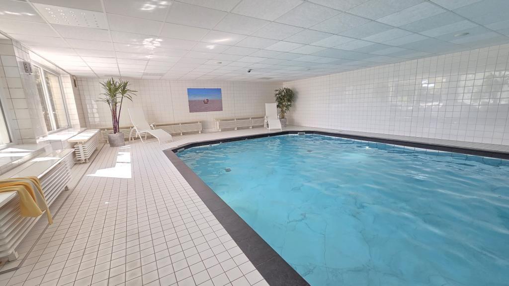 Innenpool mit weißen Fliesen und Liegestühlen an der Wand.