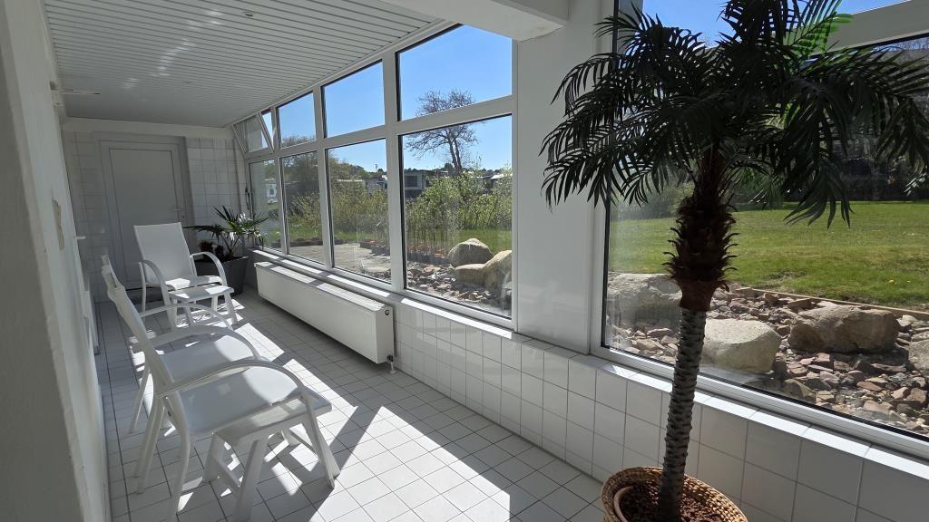 Terrasse mit weißen Stühlen und Palme. Blick auf Garten mit Steinen und Gras.