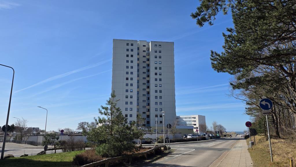 Hochhaus mit vielen Fenstern, Straße mit Bäumen und klarem Himmel.