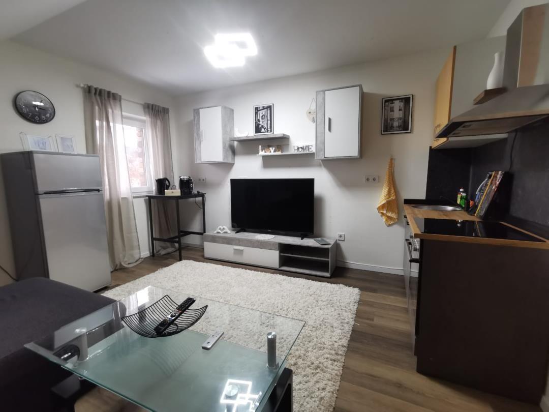 Wohnzimmer mit Küche, Fernseher, Kühlschrank und Glas-Tisch.