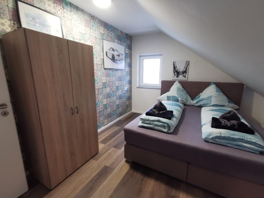 Schlafzimmer mit Doppelbett, Kleiderschrank und gemustertem Wandbezug.