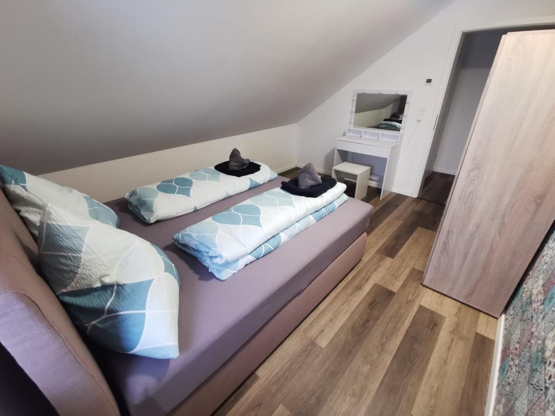 Schlafzimmer mit Doppelbett, Schrank und Schreibtisch unter Dachschräge.