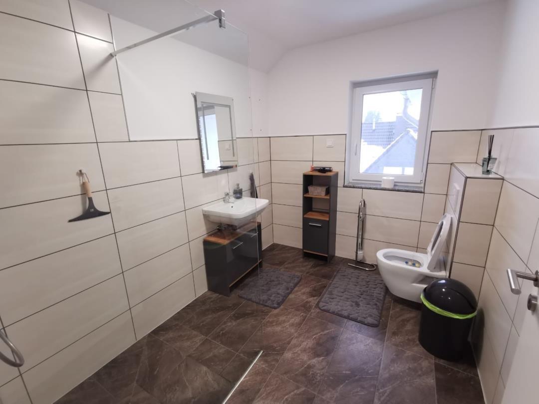 Badezimmer mit Dusche, Waschbecken und Toilette. Fenster mit Blick nach draußen.