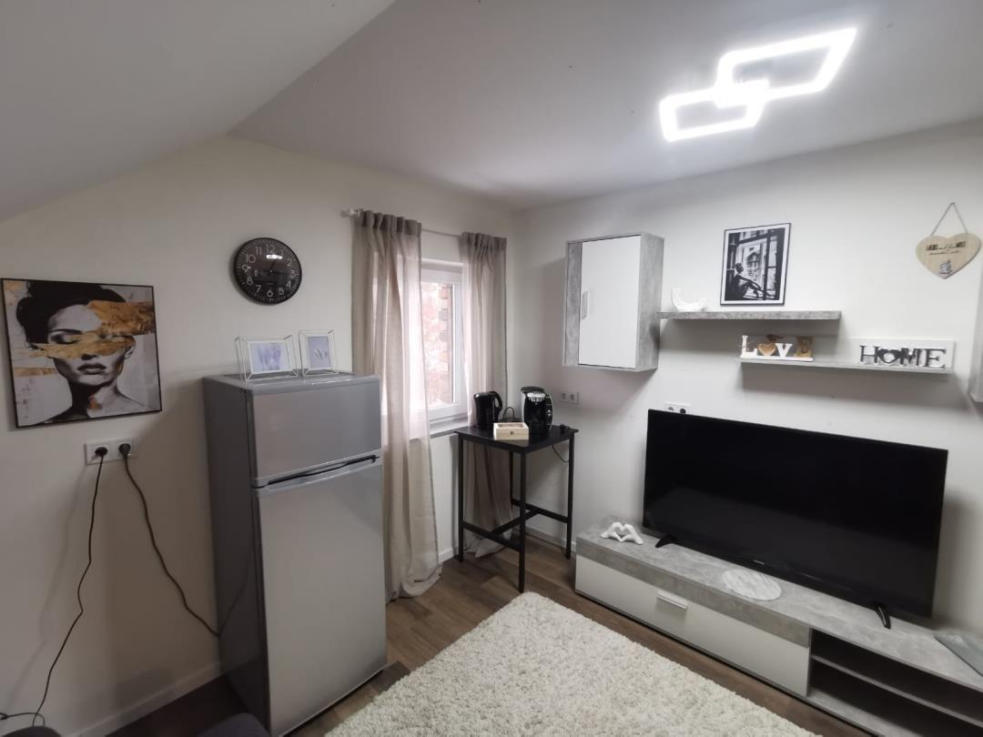 Wohnzimmer mit Fernseher, Kühlschrank und Fenster mit Vorhängen.