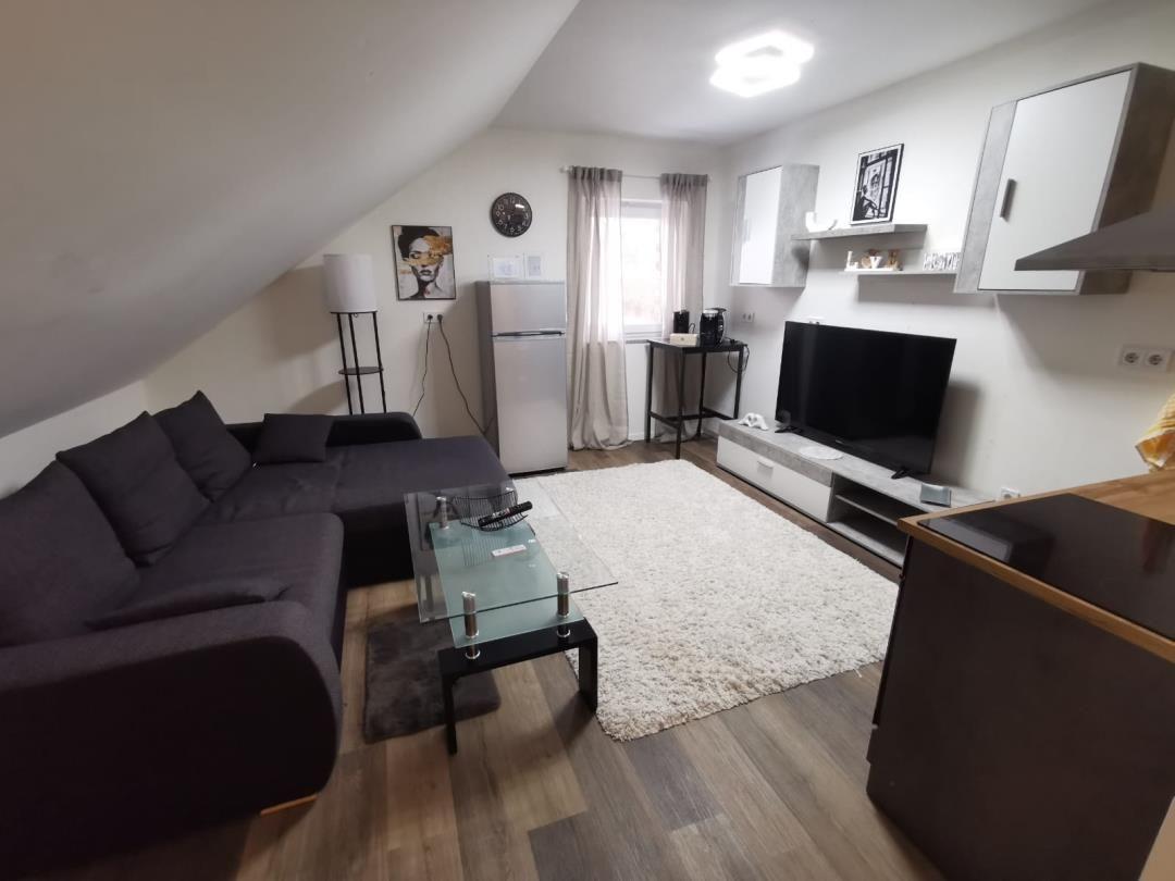 Wohnzimmer mit Sofa, Fernseher und Küchenzeile unter Dachschrägen.