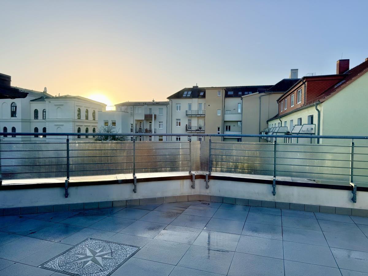 Terrasse mit Blick auf städtische Gebäude bei Sonnenuntergang. Bodenfliesen und Metallgeländer.