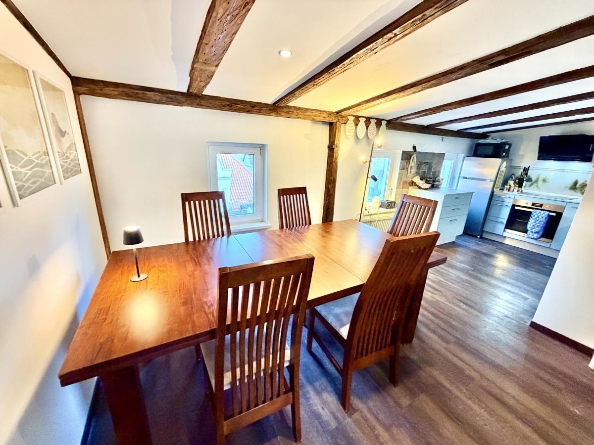 Esszimmer mit Holztisch und Stühlen, Küche im Hintergrund, Holzbalken an der Decke.