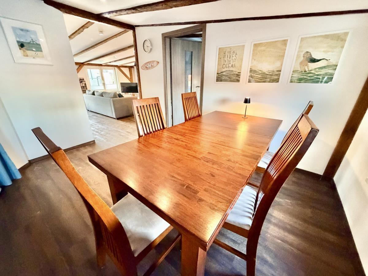 Essbereich mit Holztisch und Stühlen. Im Hintergrund Wohnzimmer mit Sofa.