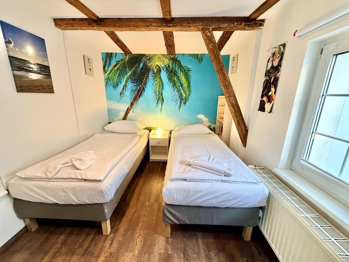 Zwei Betten mit weißer Bettwäsche, Holzdielen und Wandbildern mit Palmen.