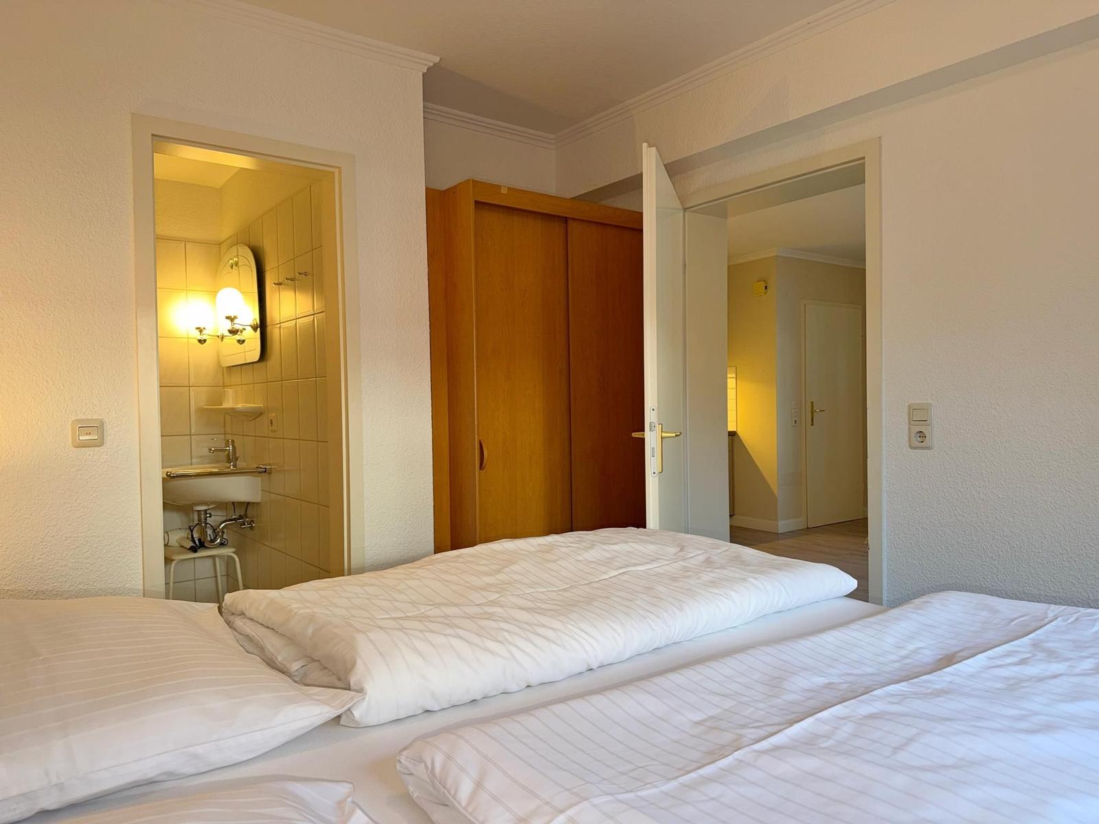 Schlafzimmer mit Bett, Kleiderschrank und Blick in Bad und Flur.