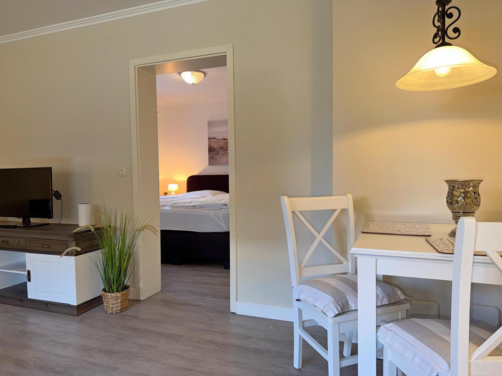 Wohnbereich mit TV, Esstisch und Blick in Schlafzimmer mit Bett.