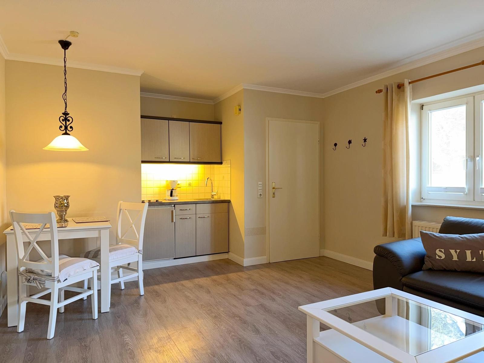 Wohnküche mit Essbereich, Sofa und Fenster. Holzboden und Küchenzeile mit Schrank.