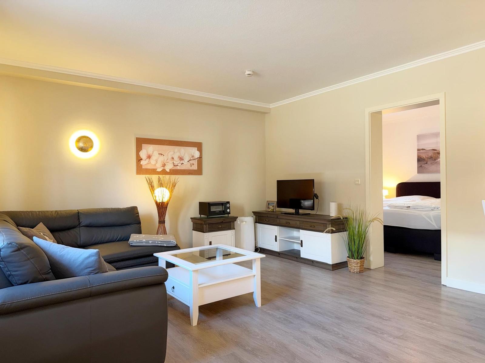 Wohnbereich mit Sofa, Couchtisch und TV. Im Hintergrund ist das Schlafzimmer sichtbar.