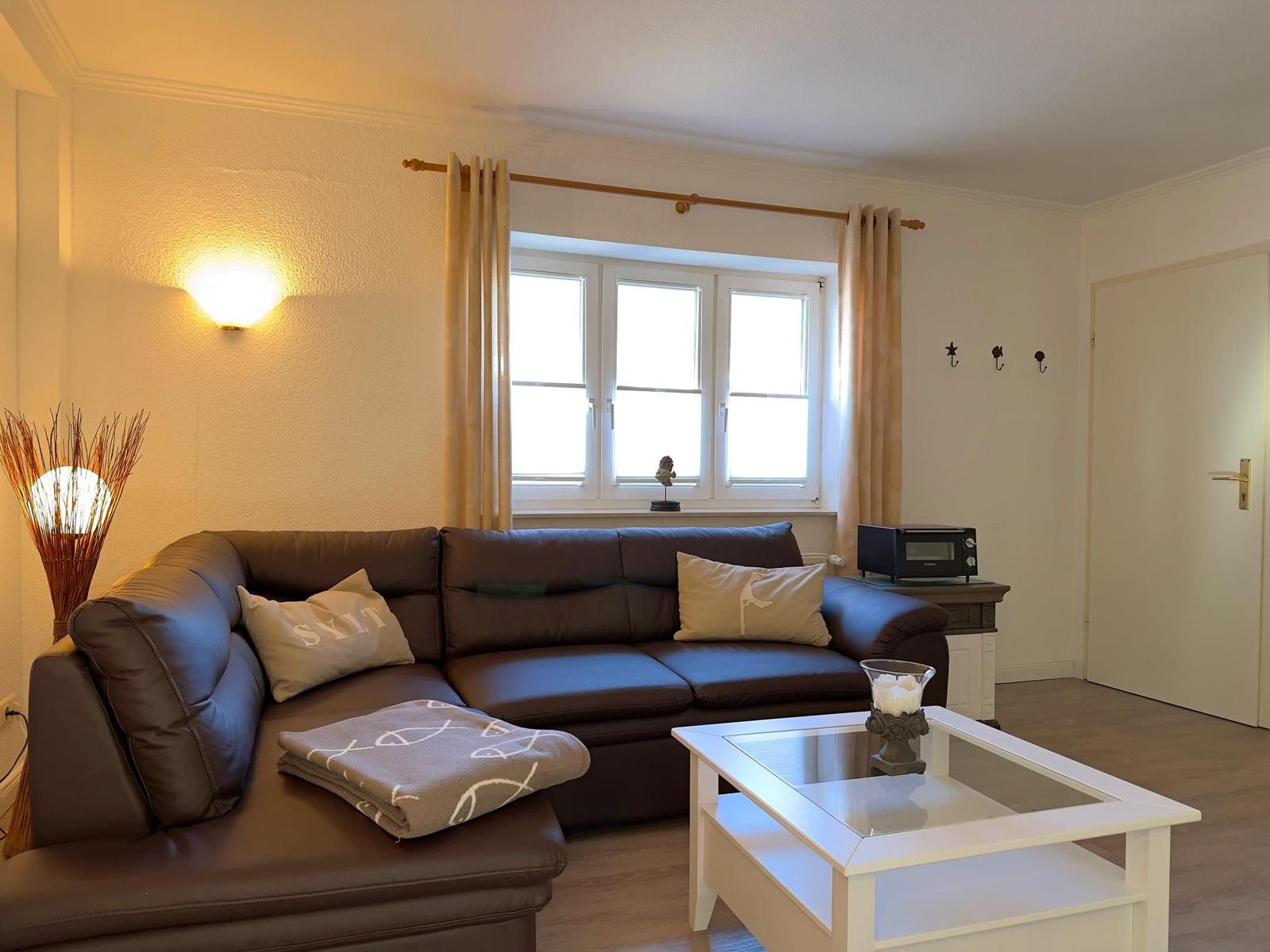 Ein Wohnzimmer mit braunem Sofa, weißem Couchtisch und Fenster mit Vorhängen.