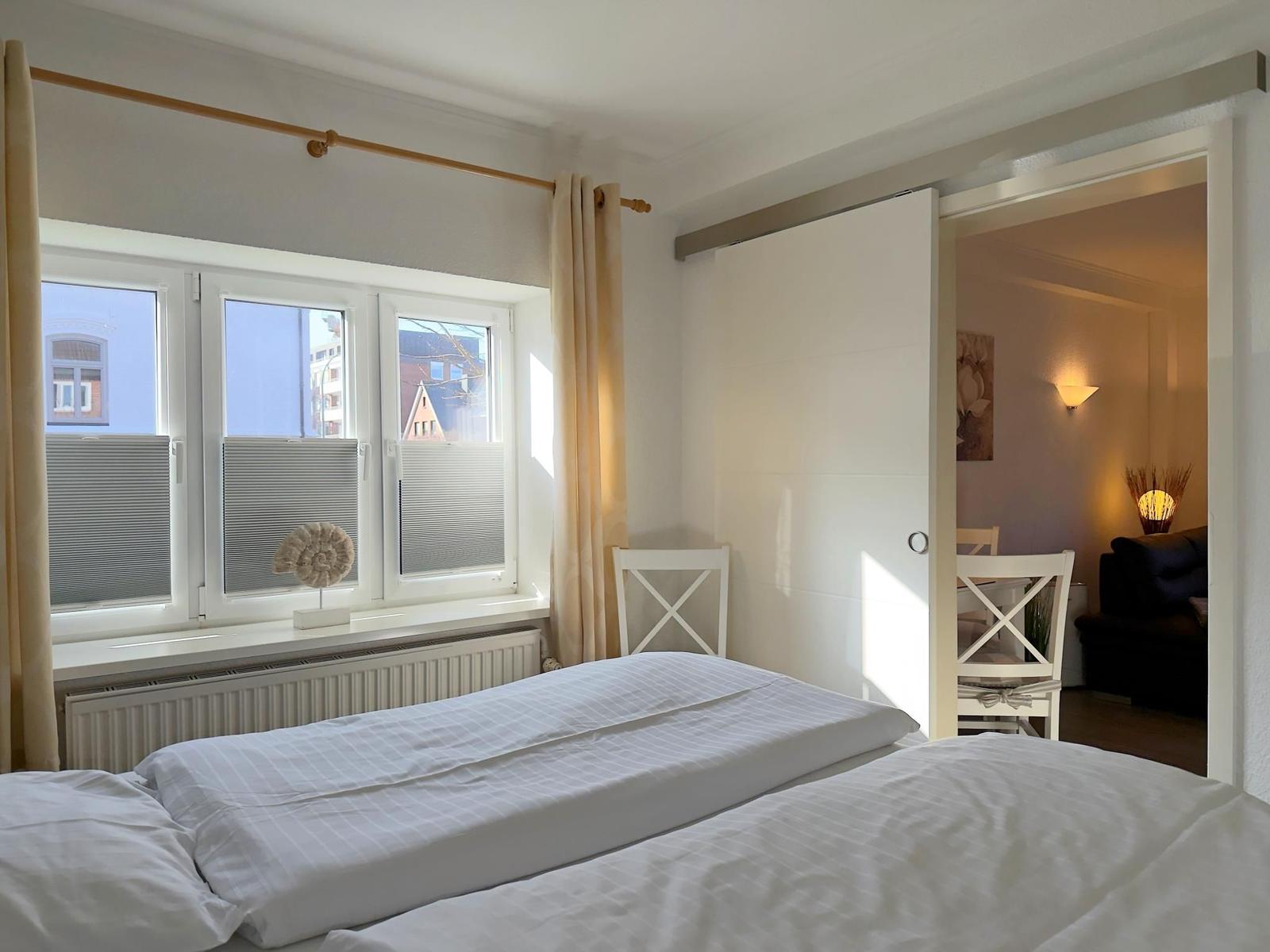 Schlafzimmer mit Bett, Fenster und Sicht in Wohnbereich.