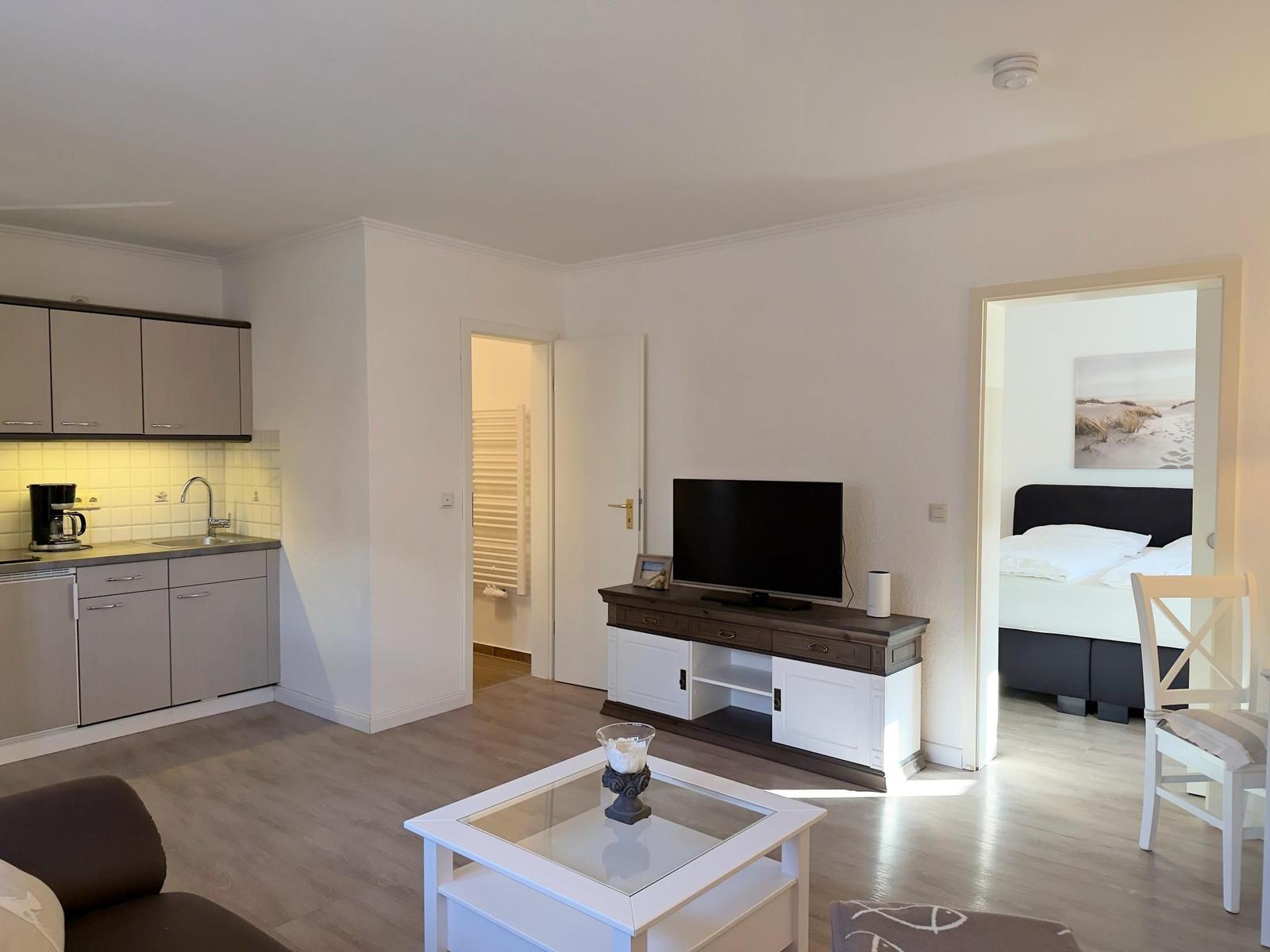 Wohnung mit Küche, Wohnzimmer und Schlafzimmer. Fernseher, Tisch und Stühle sichtbar.