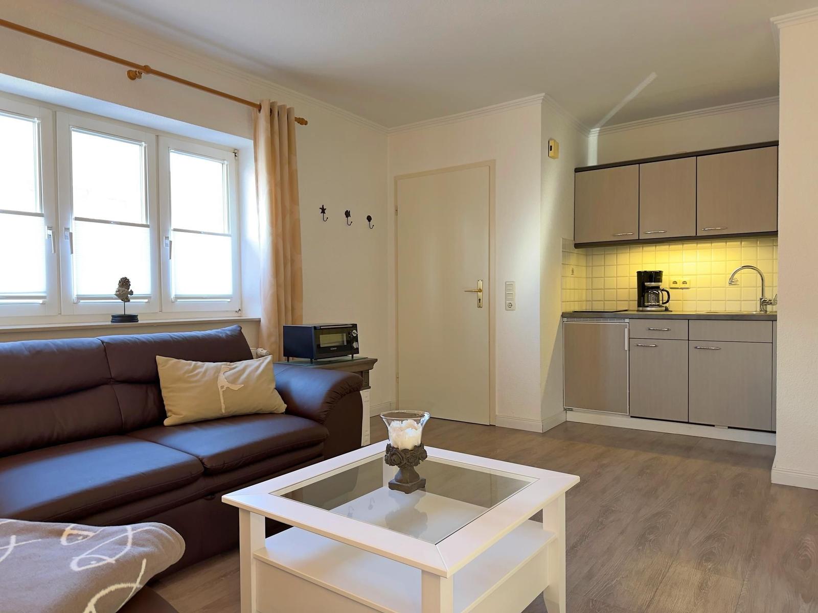 Wohnzimmer mit Sofa, Couchtisch und Küche im Hintergrund.