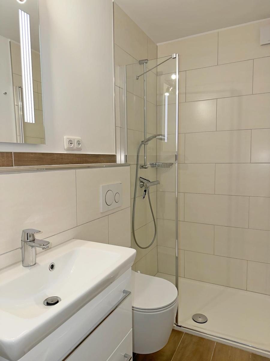 Badezimmer mit Dusche, Waschbecken und Toilette. Fliesenwand und Spiegel.