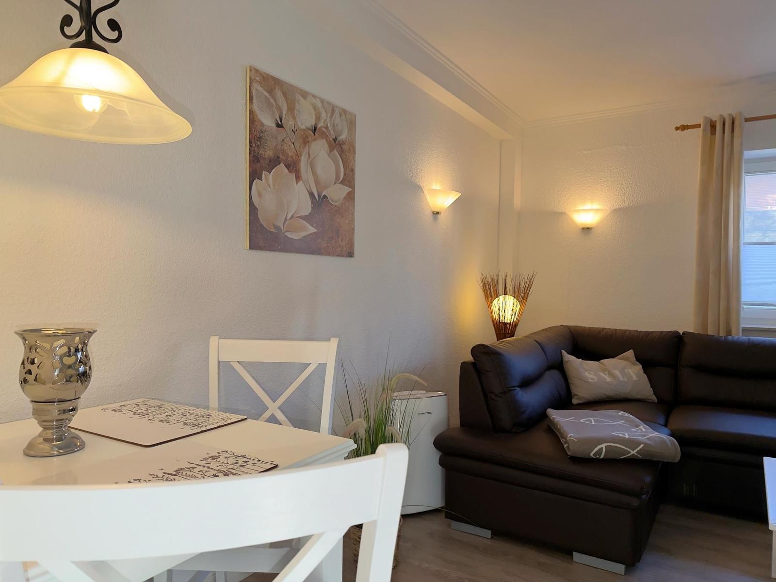 Wohn- und Essbereich mit braunem Sofa, weißen Stühlen und Wandbild mit Blumenmotiv.