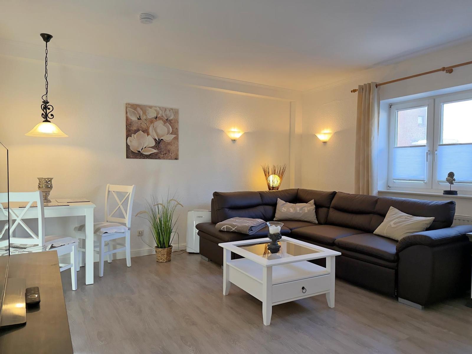 Wohnzimmer mit braunem Sofa, weißem Couchtisch und Essbereich.