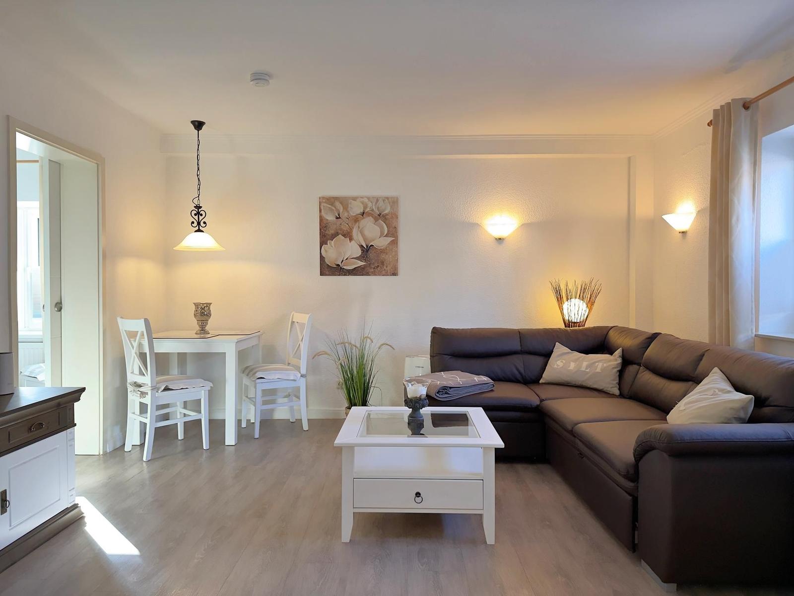 Wohn- und Essbereich mit braunem Sofa, weißem Tisch und Stühlen sowie Wandbild.