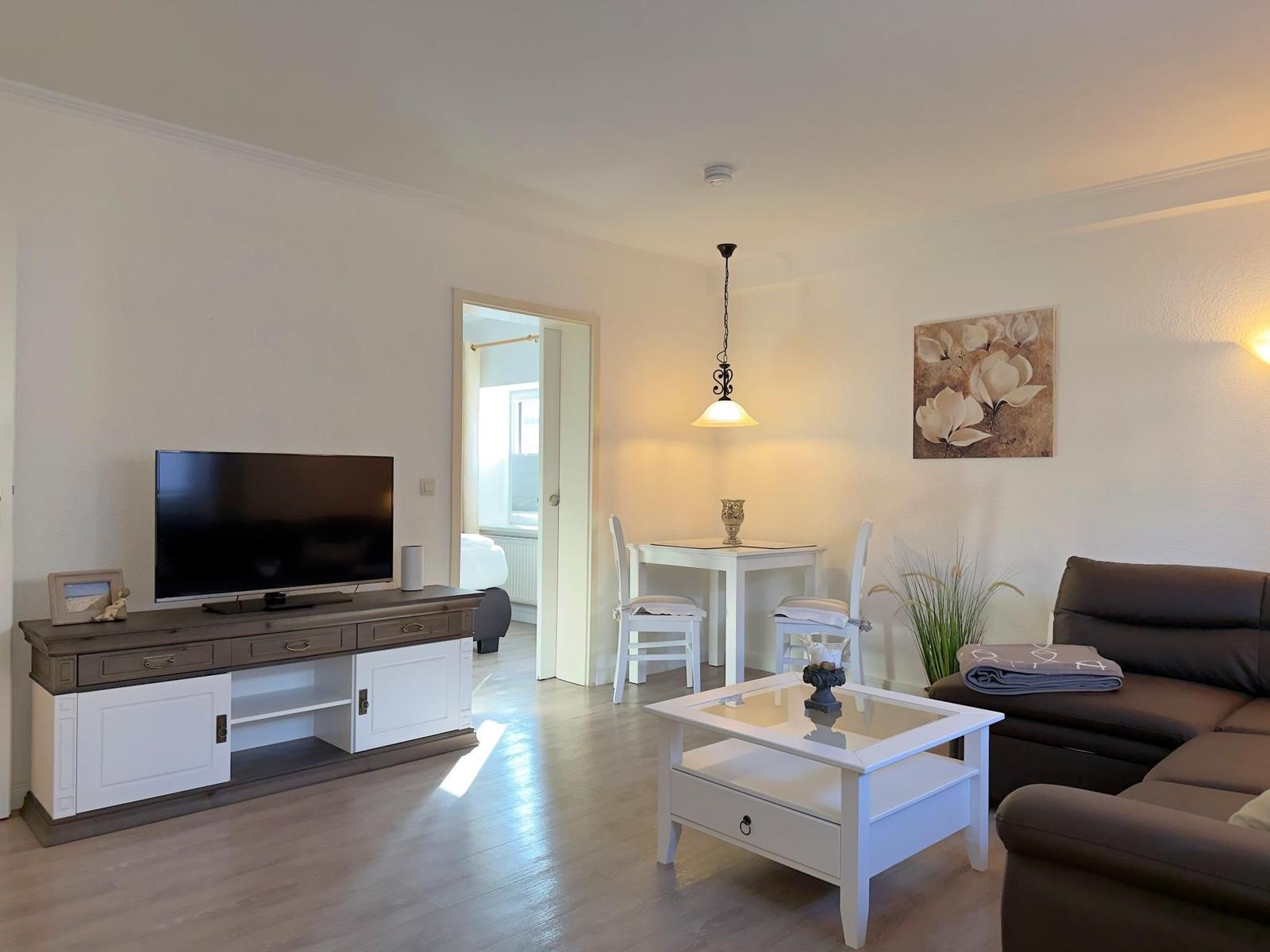 Wohnzimmer mit Sofa, Fernseher und Esstisch.
