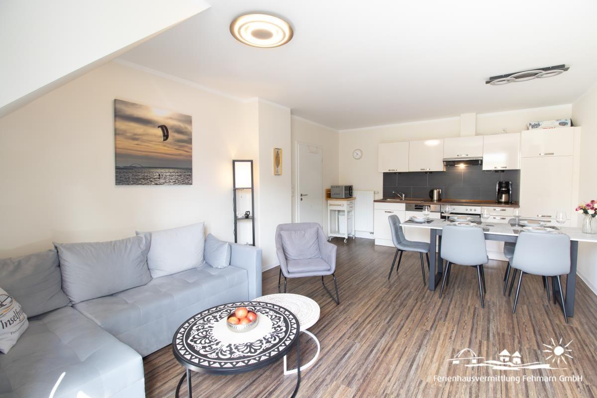 Living area with sofa, dining table, and kitchen. Wooden floor and wall picture with kitesurfer.