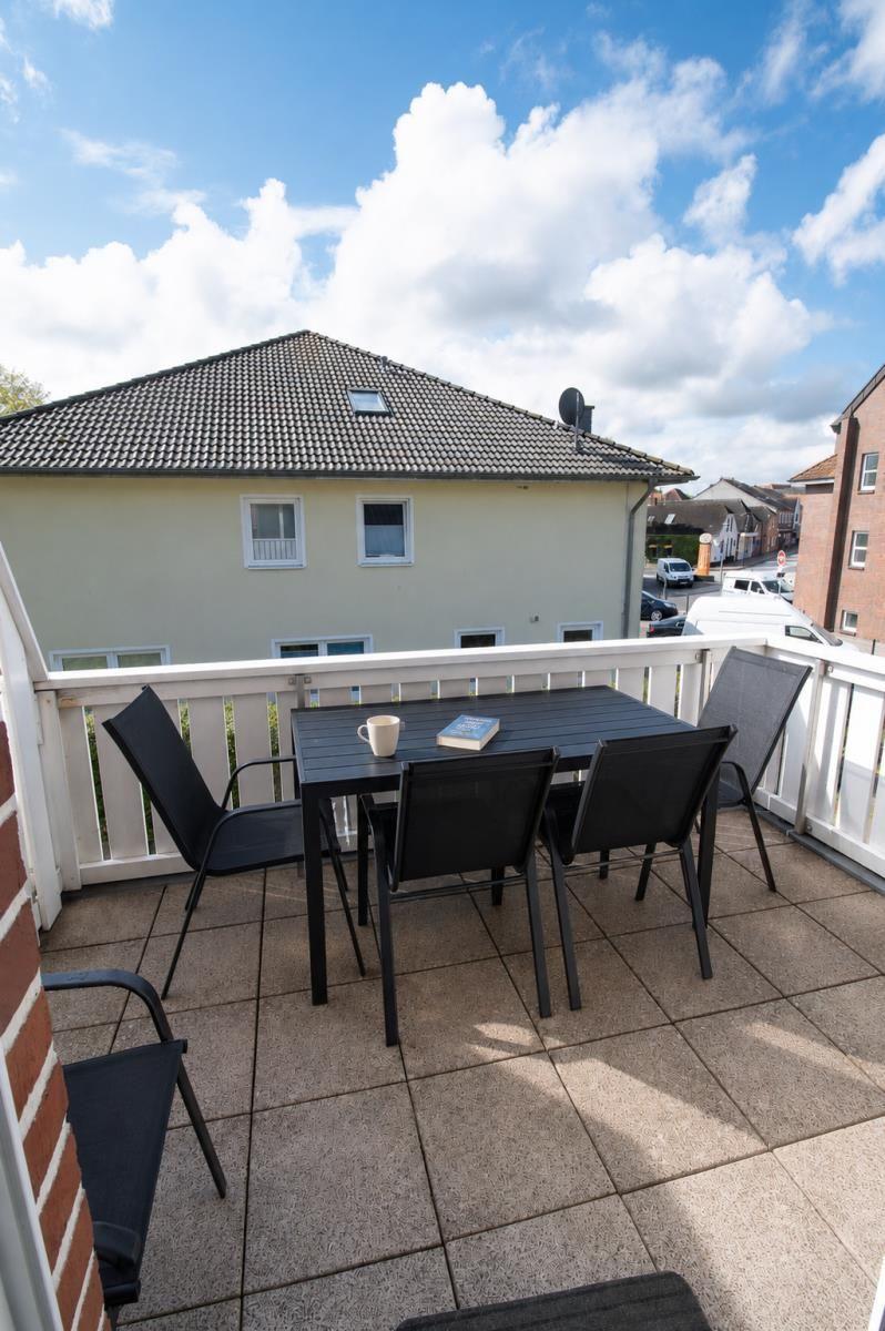 Terrace with table and chairs, view of house and street under blue sky.