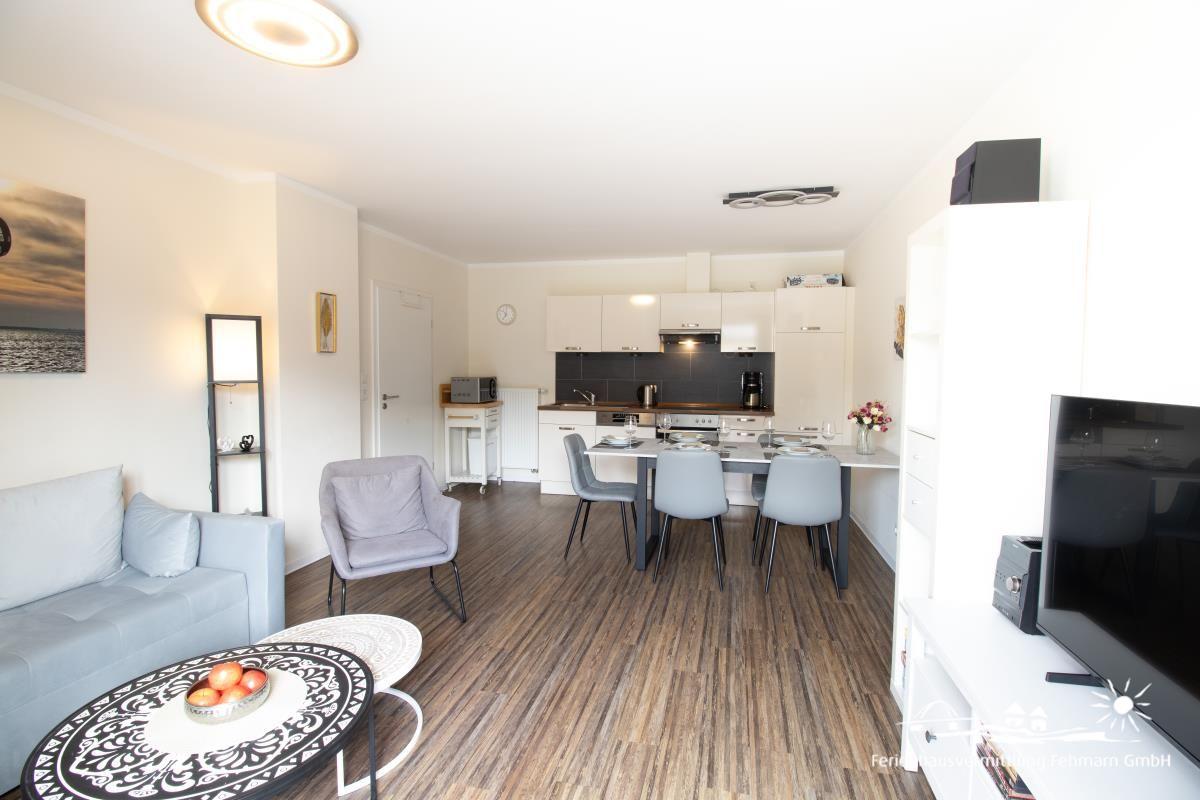 Apartment with kitchen, dining table and sofa on wooden floor.