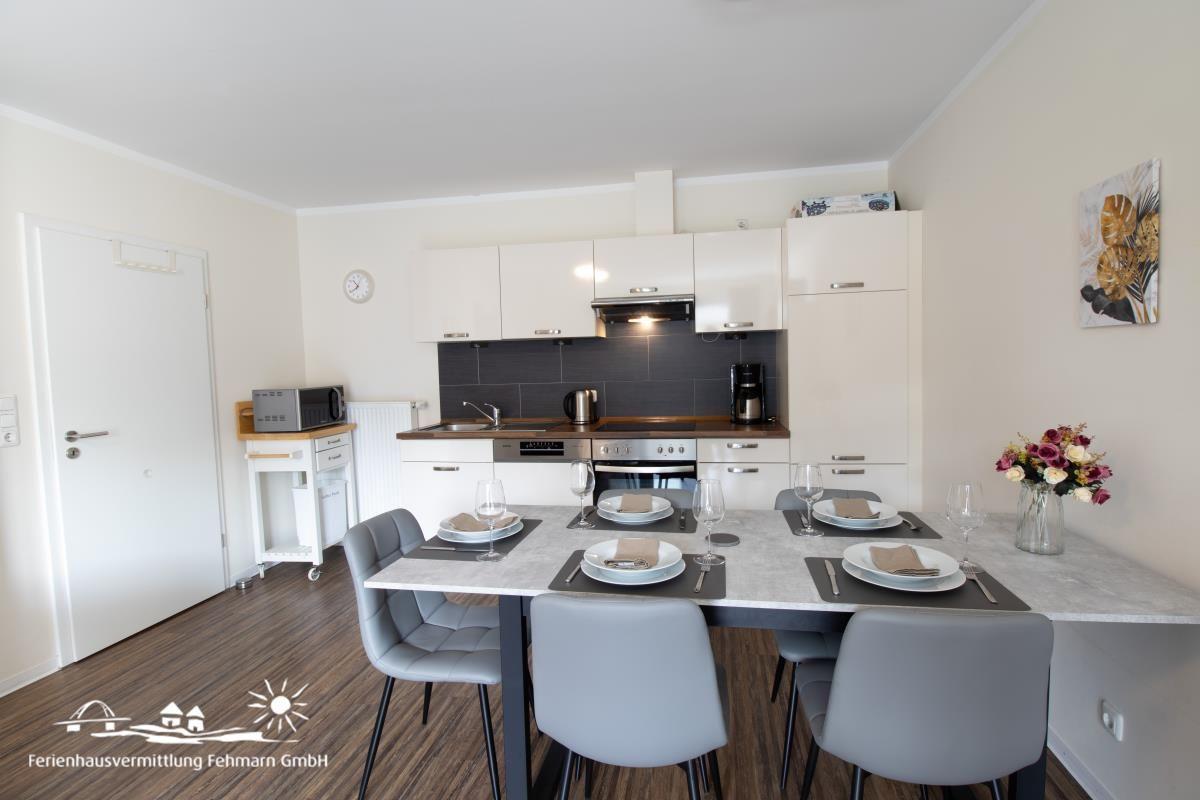 Kitchen with dining area, white cabinets, dining table with chairs and flower vase.