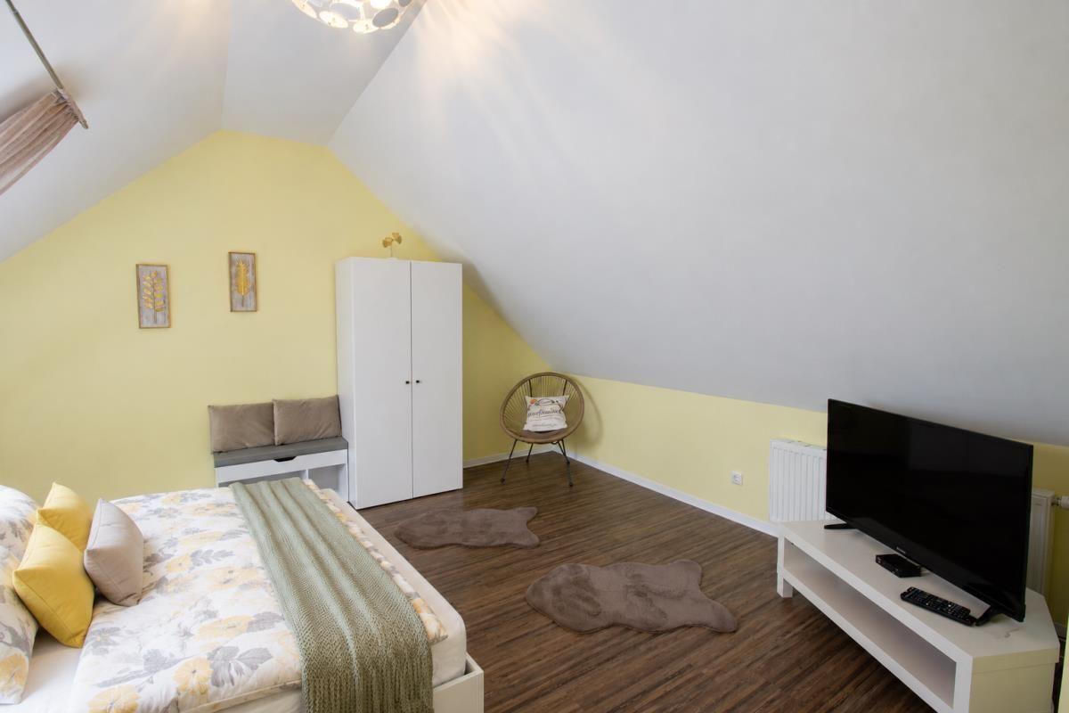 Bedroom with bed, wardrobe, chair, and TV. Wooden floor and yellow wall.