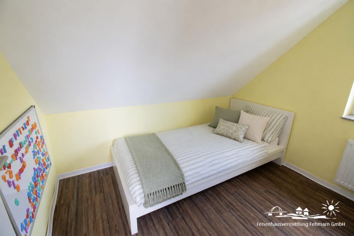 Bedroom with sloped ceiling, white bed, and yellow walls. Wooden floor and whiteboard on the wall.