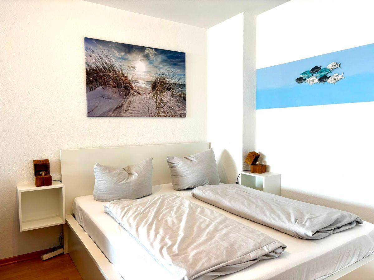 Zimmer mit Doppelbett, Wandbild Strand und Fischdekoration.