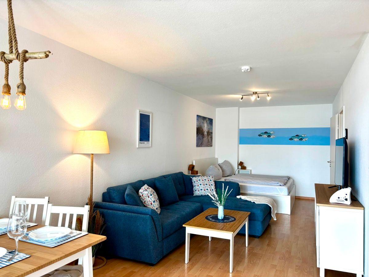Wohnbereich mit Sofa, Esstisch und Bett im Hintergrund.