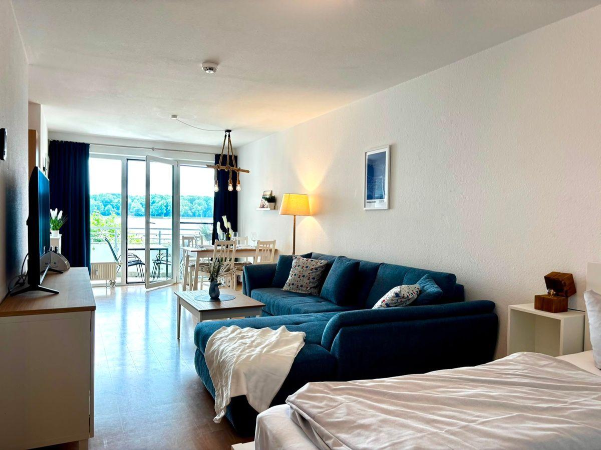 Wohnbereich mit Sofa, Bett und Blick auf den See